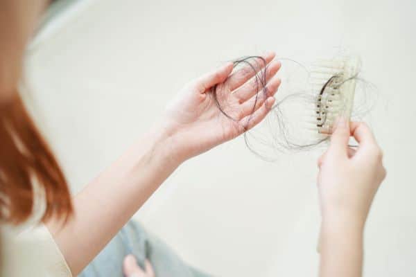 Mulher segurando fios de cabelo que caíram após realização de cirurgia plástica.