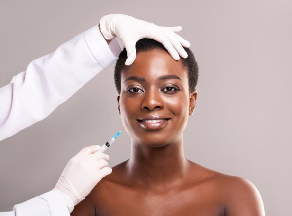 Jovem e bela mulher negra fazendo tratamento estético facial com a aplicação de bioestimulador de colágeno.