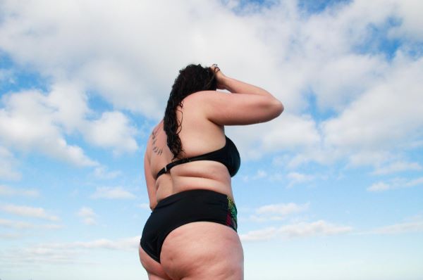 Mulher obesa, de biquini preto, aproveita o dia de céu azul e nuvens.