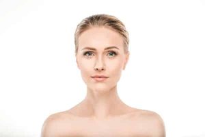 Rosto de uma mulher madura, bonita, com olhos azuis e os cabelos presos. Cuidados com a pele antes e depois de procedimentos faciais.