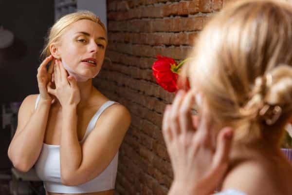 Mulher jovem e loira, com os cabelos presos, cuida das cicatrizes no terço inferior da face com Taping.