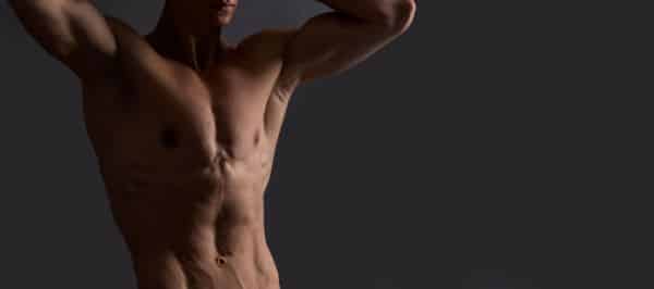 Torso superior de um belo homem jovem que tem os braços levantados sobre a cabeça.