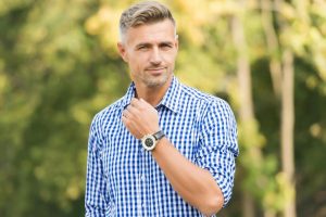 Homem bonito de meia idade, com cabelo e barba grisalhos, vestindo uma camisa xadrez azul e branca.