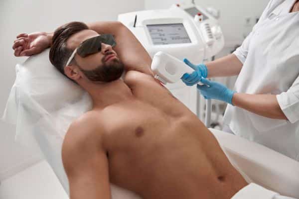 Homem com óculos de proteção e peito nu é submetido a procedimento de depilação a laser.