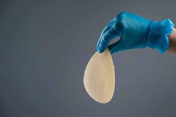 Mão de cirurgião plástico com luva azul segurando uma prótese de silicone.