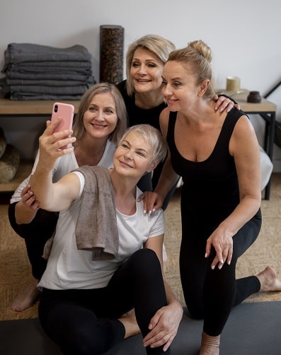 Mulheres de diferentes idades, em ambiente de atividade física, vestindo roupas apropriadas, posam para selfie. 
O envelhecimento saudável envolve cuidados não apenas estéticos, mas também físicos.