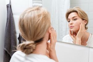 Mulher madura olhando atentamente seu rosto no espelho.